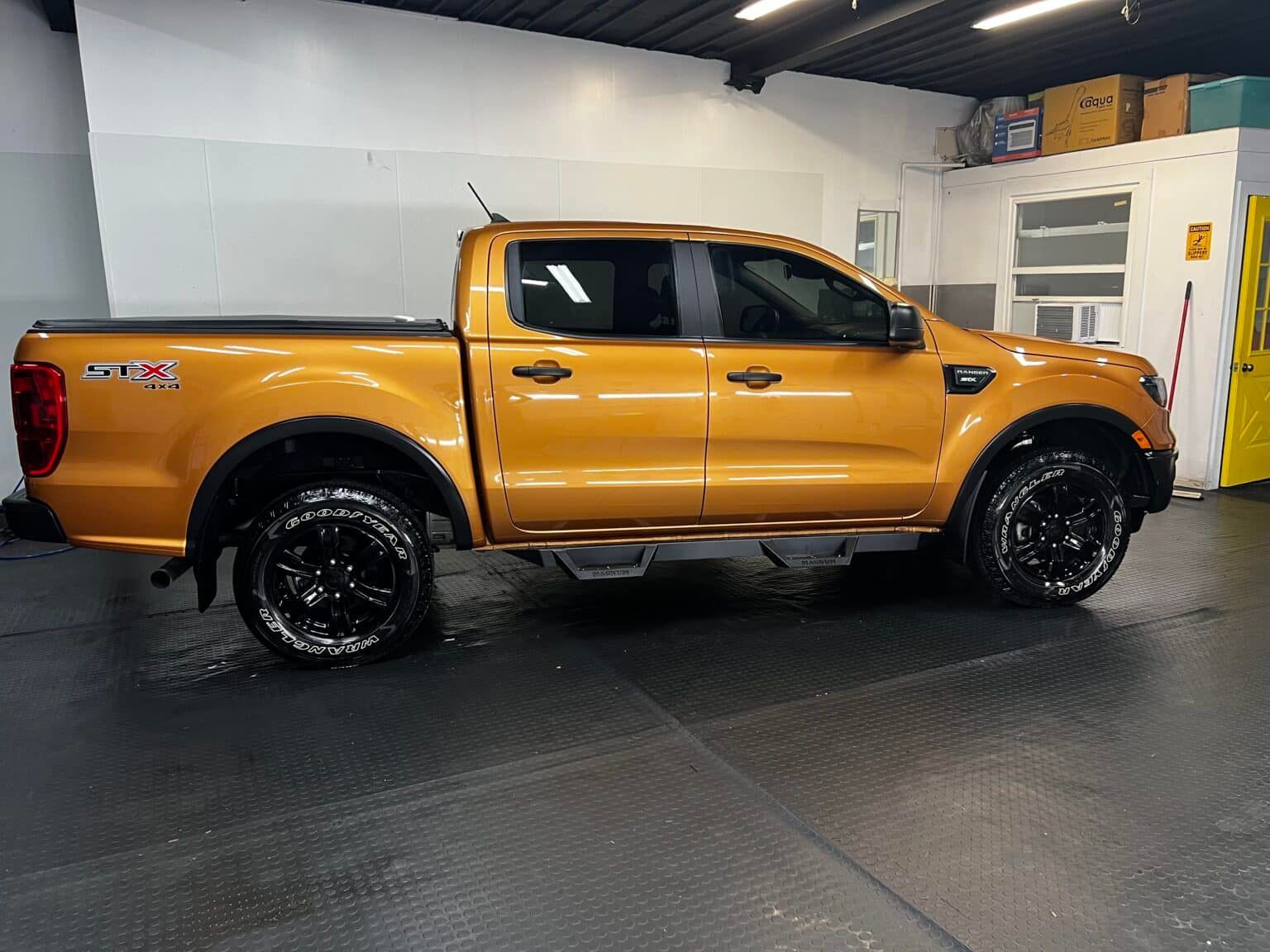 Orange pickup truck parked indoors on a black floor in a garage or showroom.