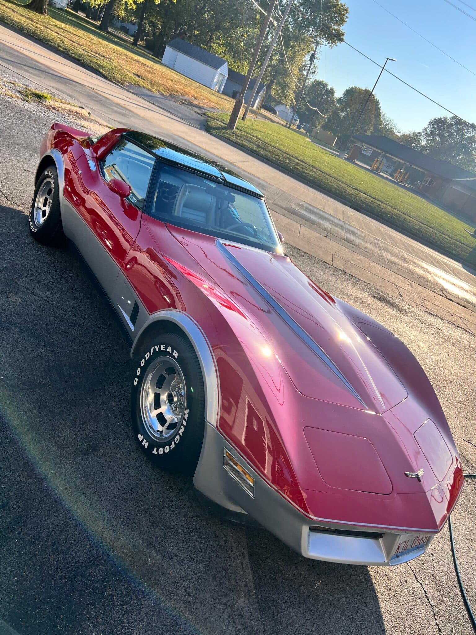 Red classic sports car parked on pavement in bright sunlight, viewed from the front-left.