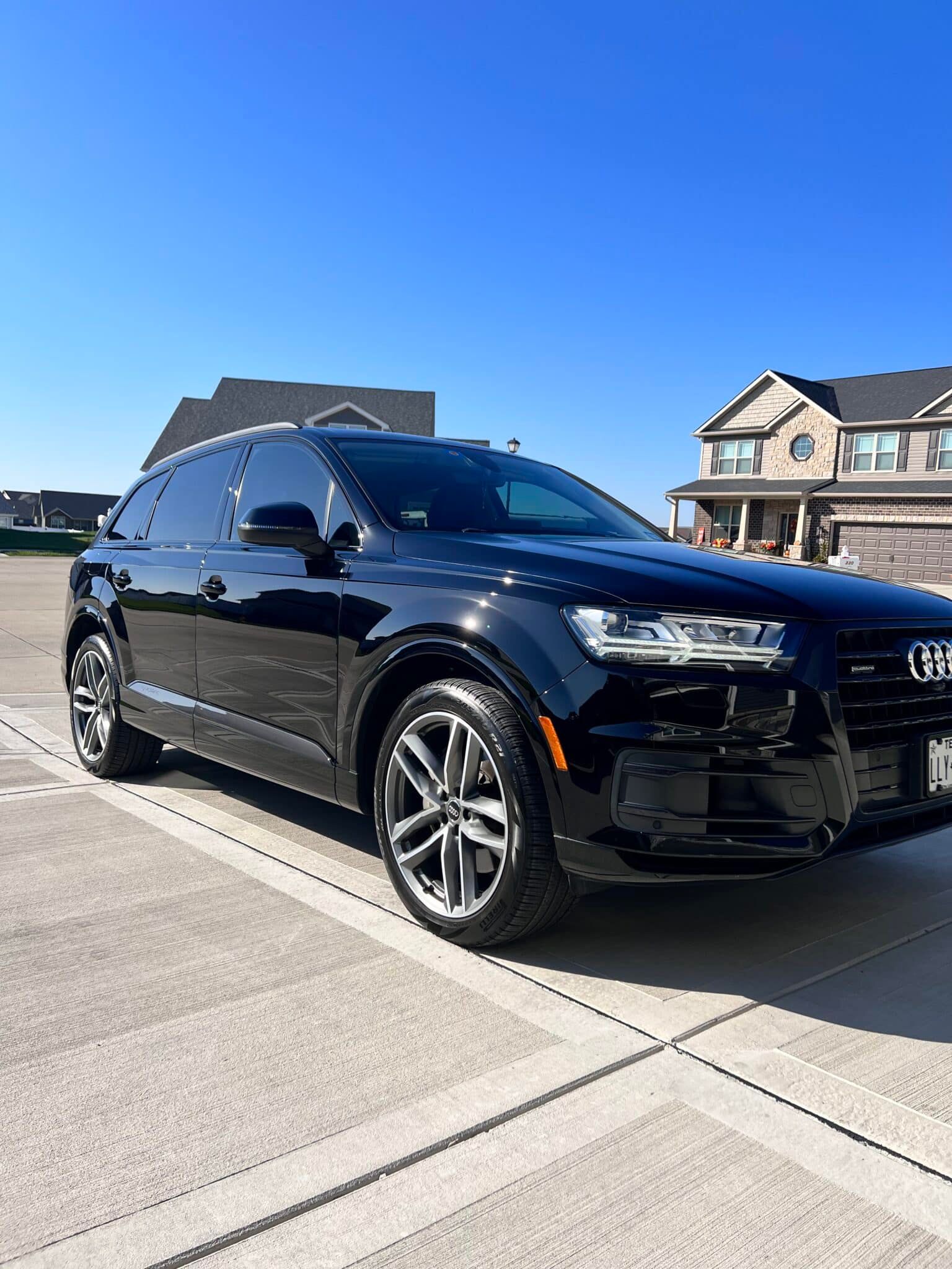 Black Audi SUV parked on a sunny driveway in front of suburban houses.