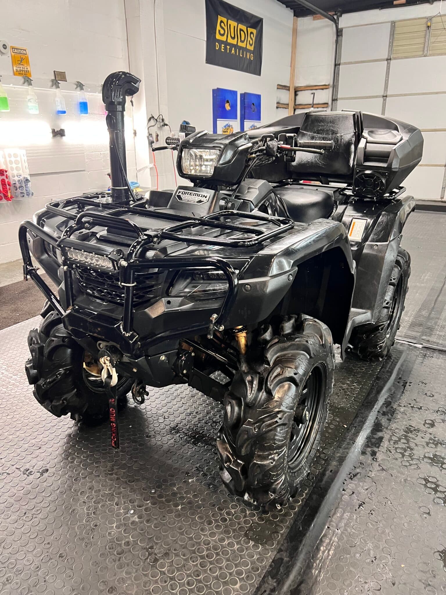 Black ATV being washed in an auto detail shop, wet floor and foam on the vehicle
