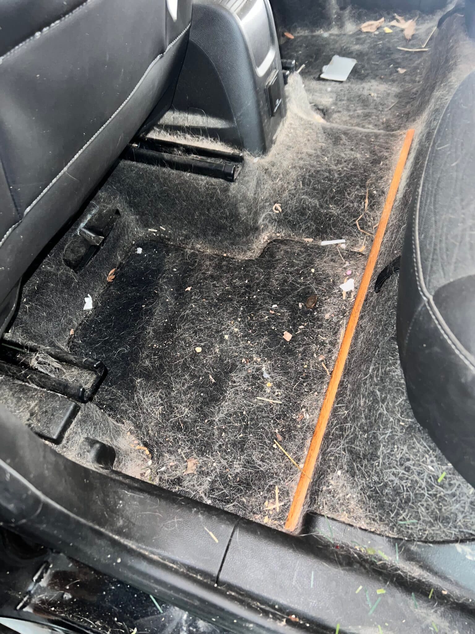 Car interior rear floor area covered in dirt and debris, with black seats and an orange trim line.