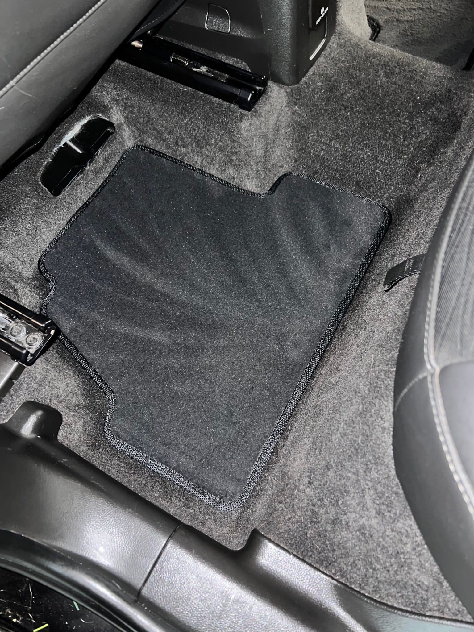 Car floor with a black mat over gray carpet next to the seat and center console