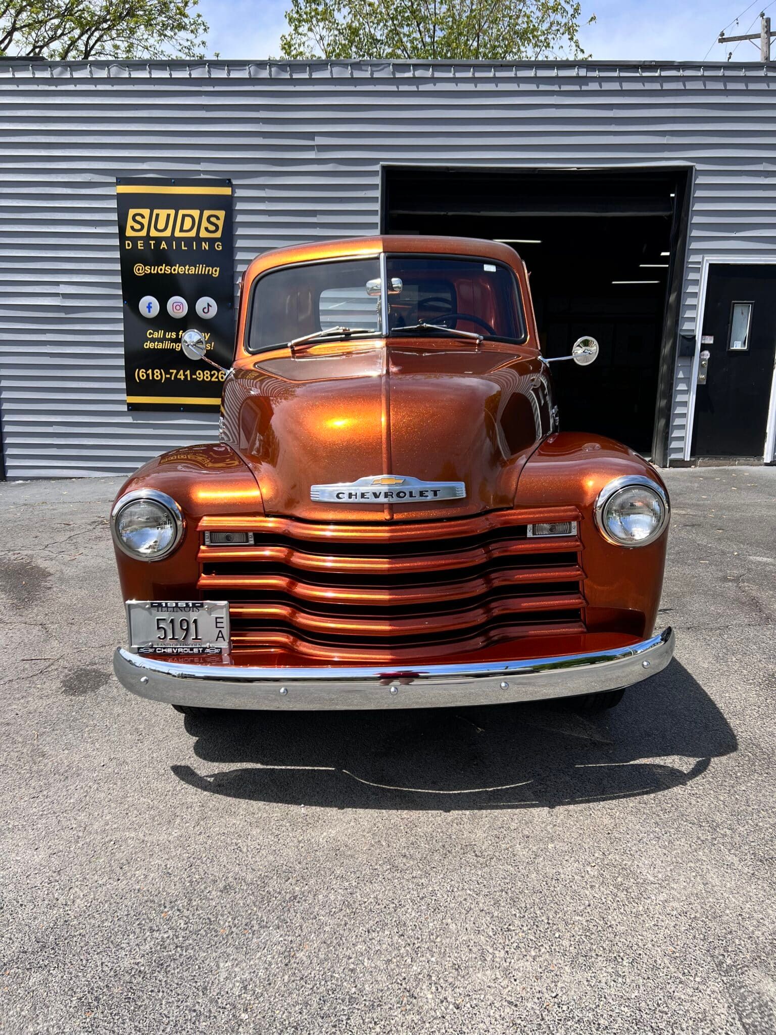 Front view of a rusty orange vintage pickup truck parked outside a garage