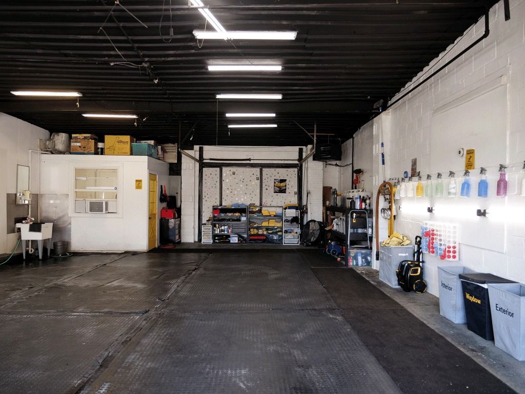 Empty warehouse interior with white walls, high ceiling lights, and storage shelves along the back and right walls