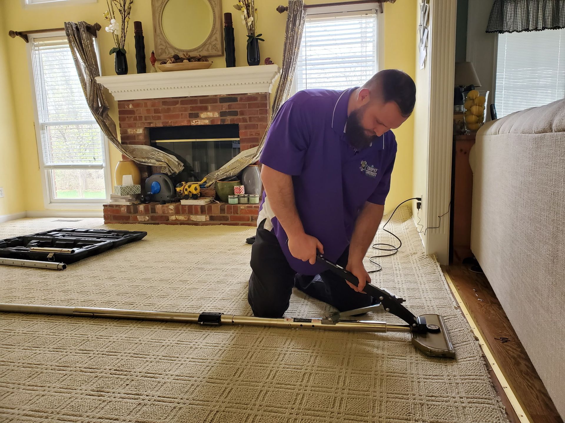 A man is cleaning a carpet in a living room with a vacuum cleaner.