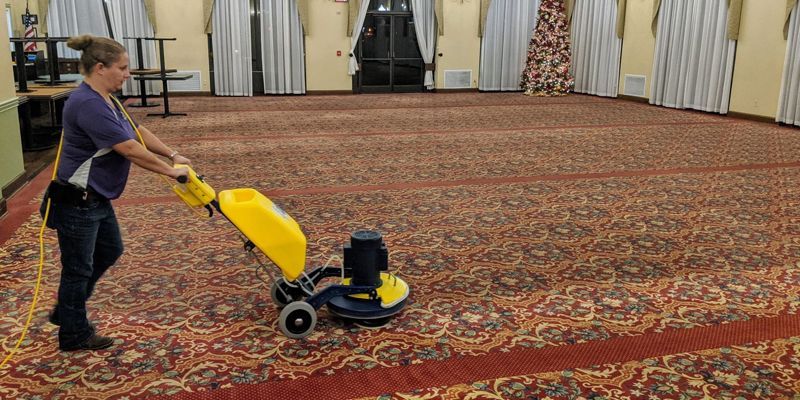 A woman is using a machine to clean a carpet in a large room.