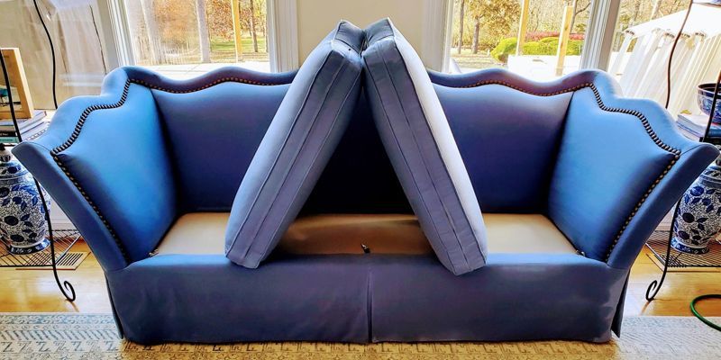 A blue couch with two pillows on it is sitting in front of a window.