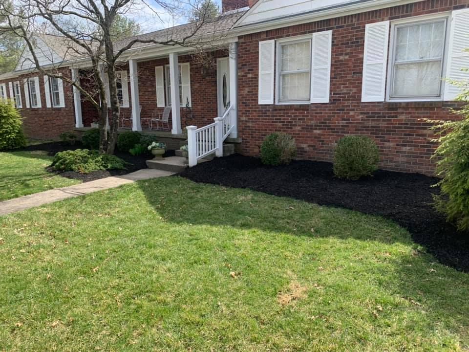 A brick house with white shutters and a large lawn in front of it.