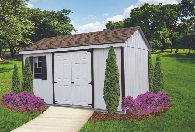 White storage shed with brown roof and landscaping in a yard.