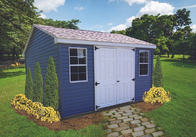 Blue shed with white doors and two windows, surrounded by green grass and landscaping.