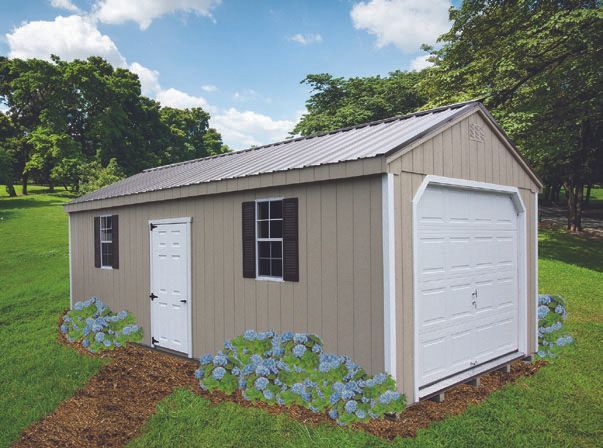 Tan shed with white door, garage door, and windows, on a green lawn with blue flowers.