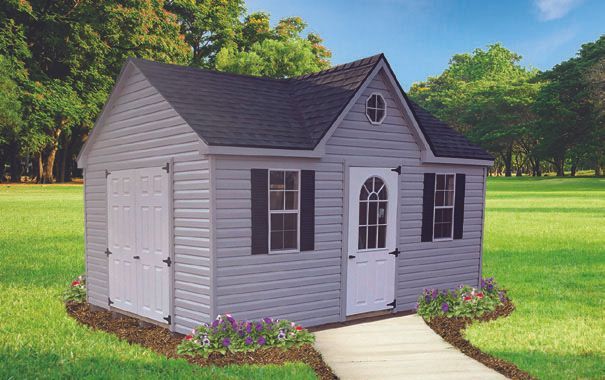 Gray shed with white doors, shutters, and trim. Walkway leads to arched door.