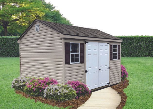 Tan storage shed with white doors, brown shutters, and flowers along a walkway in a yard.