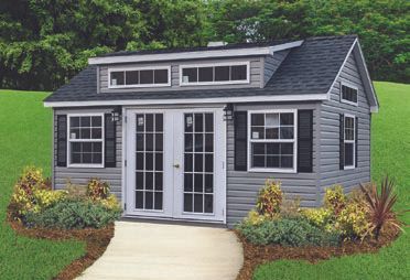 Gray shed with black shutters, double doors, and dormer windows, on a green lawn.