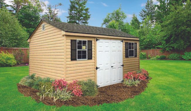 Tan shed with white double doors, two windows, black shutters, and a garden.