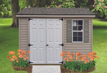 Tan shed with white double doors, small window, and orange flowers in front.