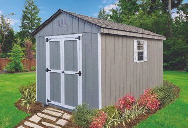 Gray shed with double doors and window in a garden setting, surrounded by landscaping.
