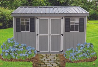 Gray shed with double doors, two windows with black shutters, and metal roof. Blue hydrangeas in front.