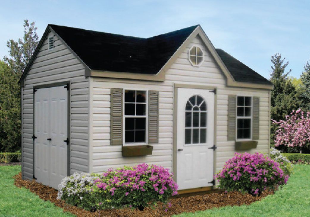 Tan shed with black roof, white door, and shutters. Surrounded by purple flowers, grass, and trees.