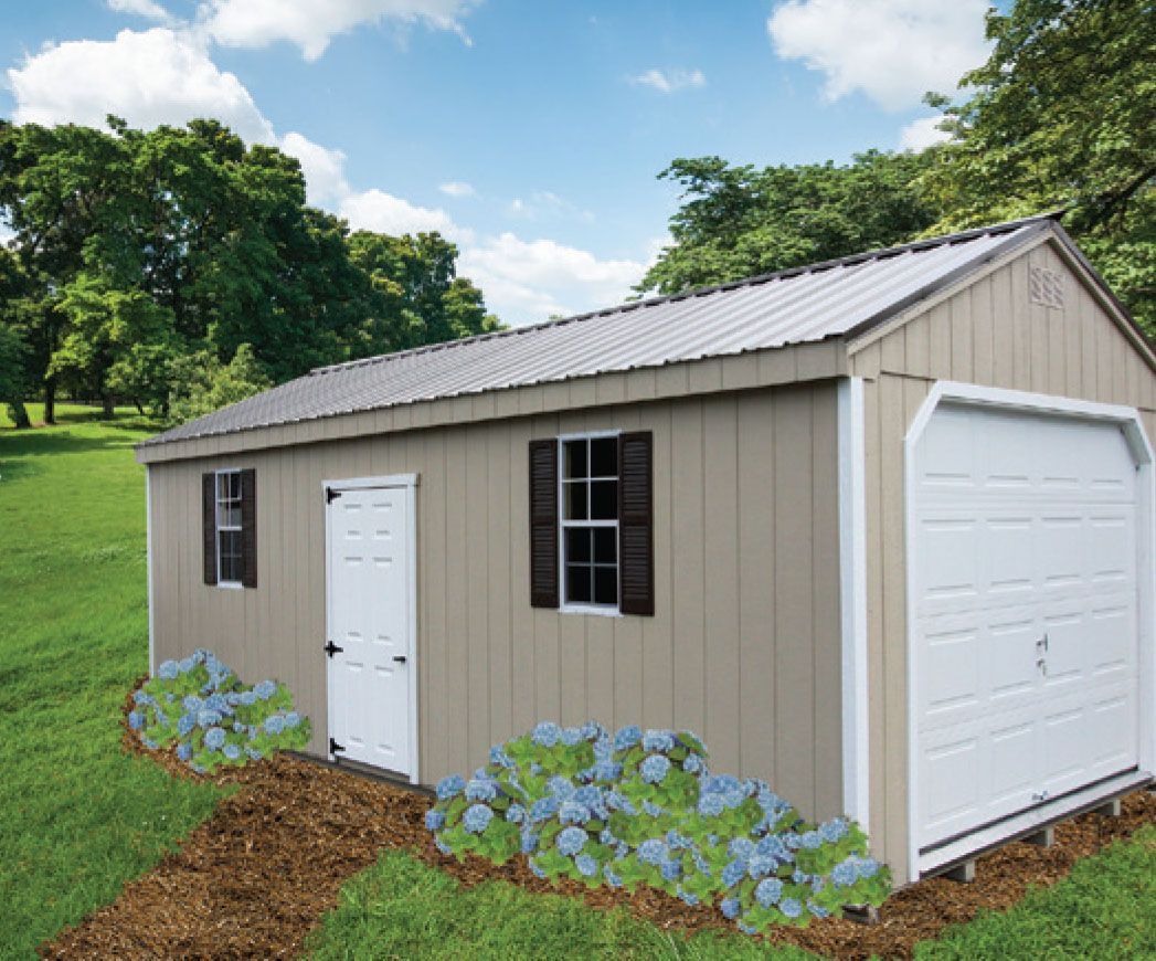 Tan shed with a garage door, a white door, and shutters. Surrounded by grass, plants, and trees.