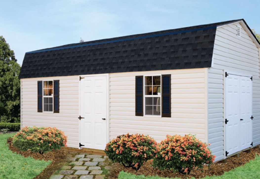 White shed with black roof, door, window, and shutters, small bushes, a stone path, and a green lawn.
