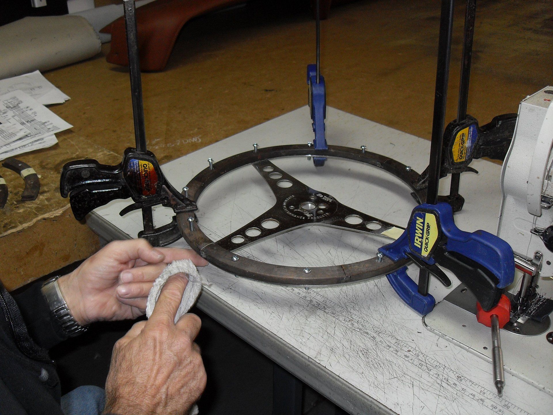 A man is working on a steering wheel with blue clamps.