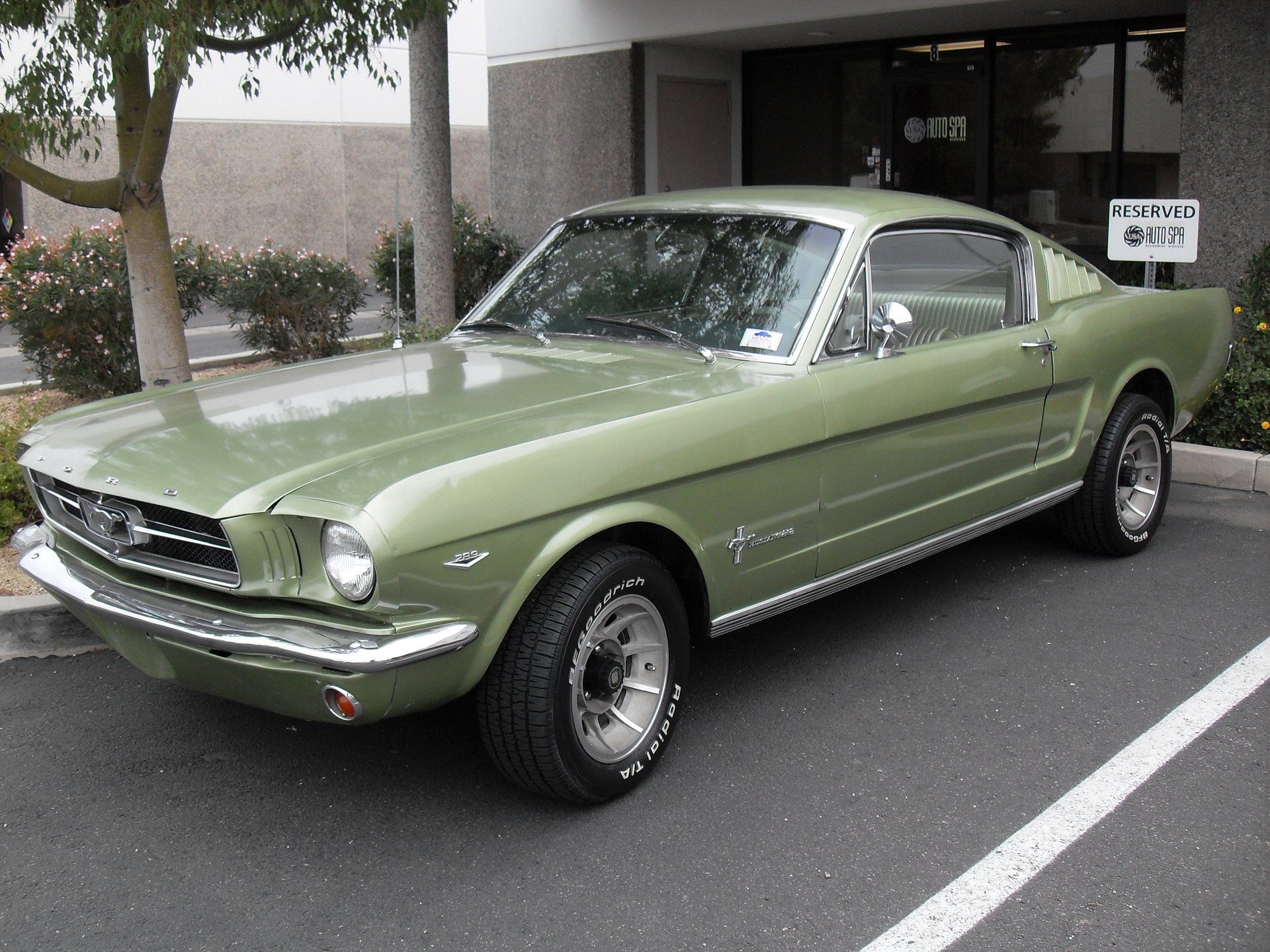 A green mustang is parked in front of a building.