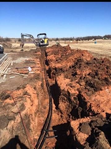 Construction site: excavator digging trench, laying black cables. Sunny day, brown soil.