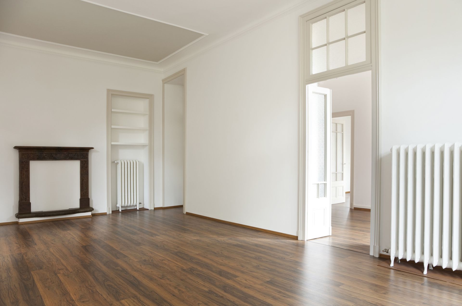 Empty room with hardwood floors, white walls, and a fireplace.