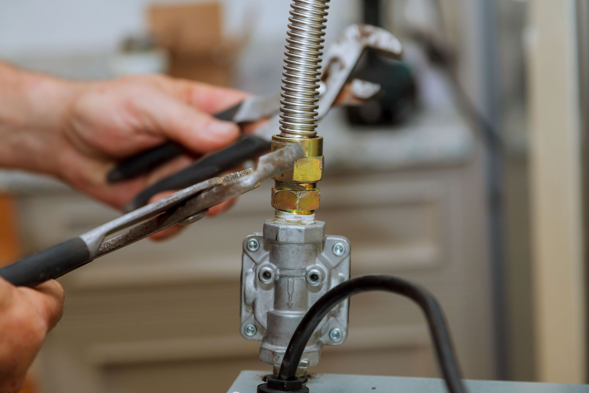 Person using pliers to tighten a gas line fitting with a wrench. Indoors, close-up shot.
