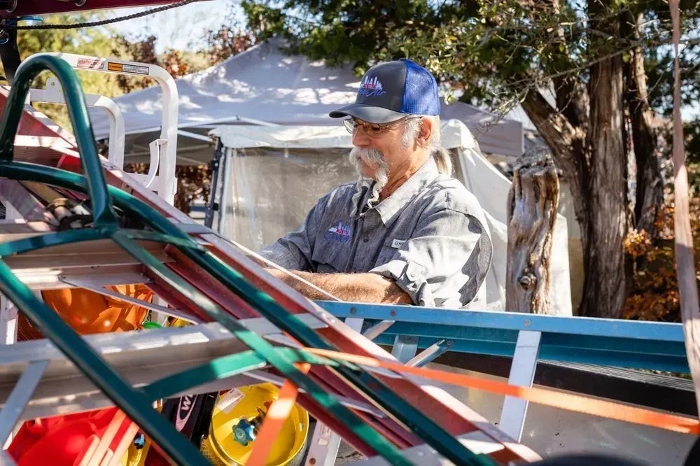 Man in a blue cap and gray shirt works on a colorful cart outdoors.