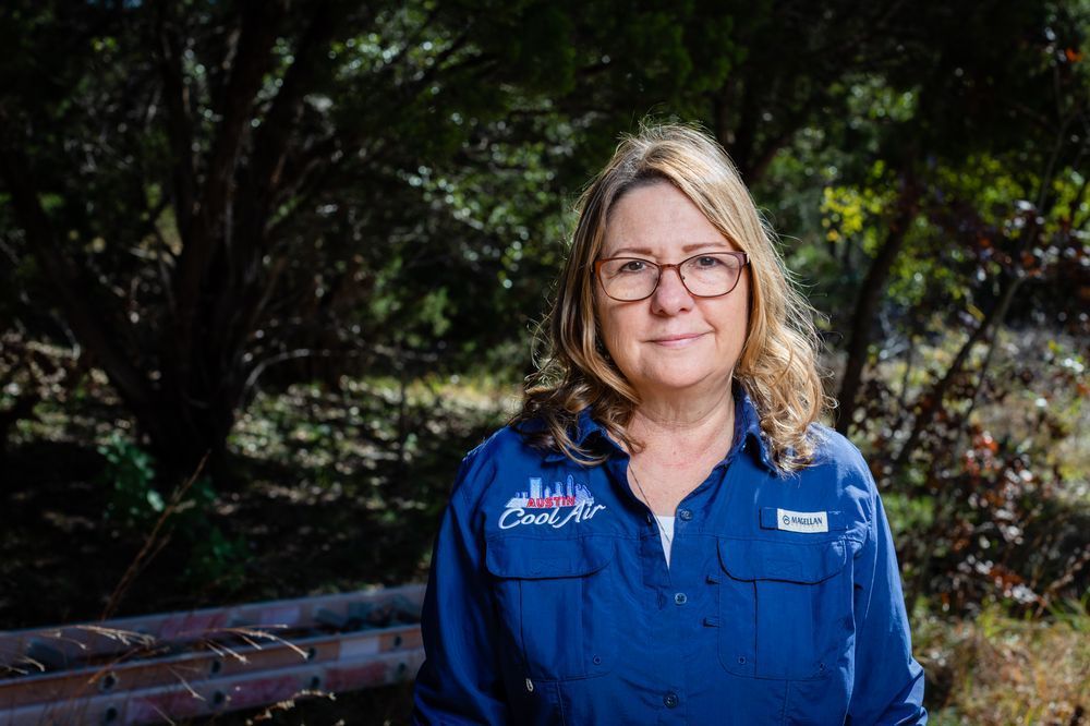 Woman with glasses, blue shirt, outdoor setting; smiling at camera.