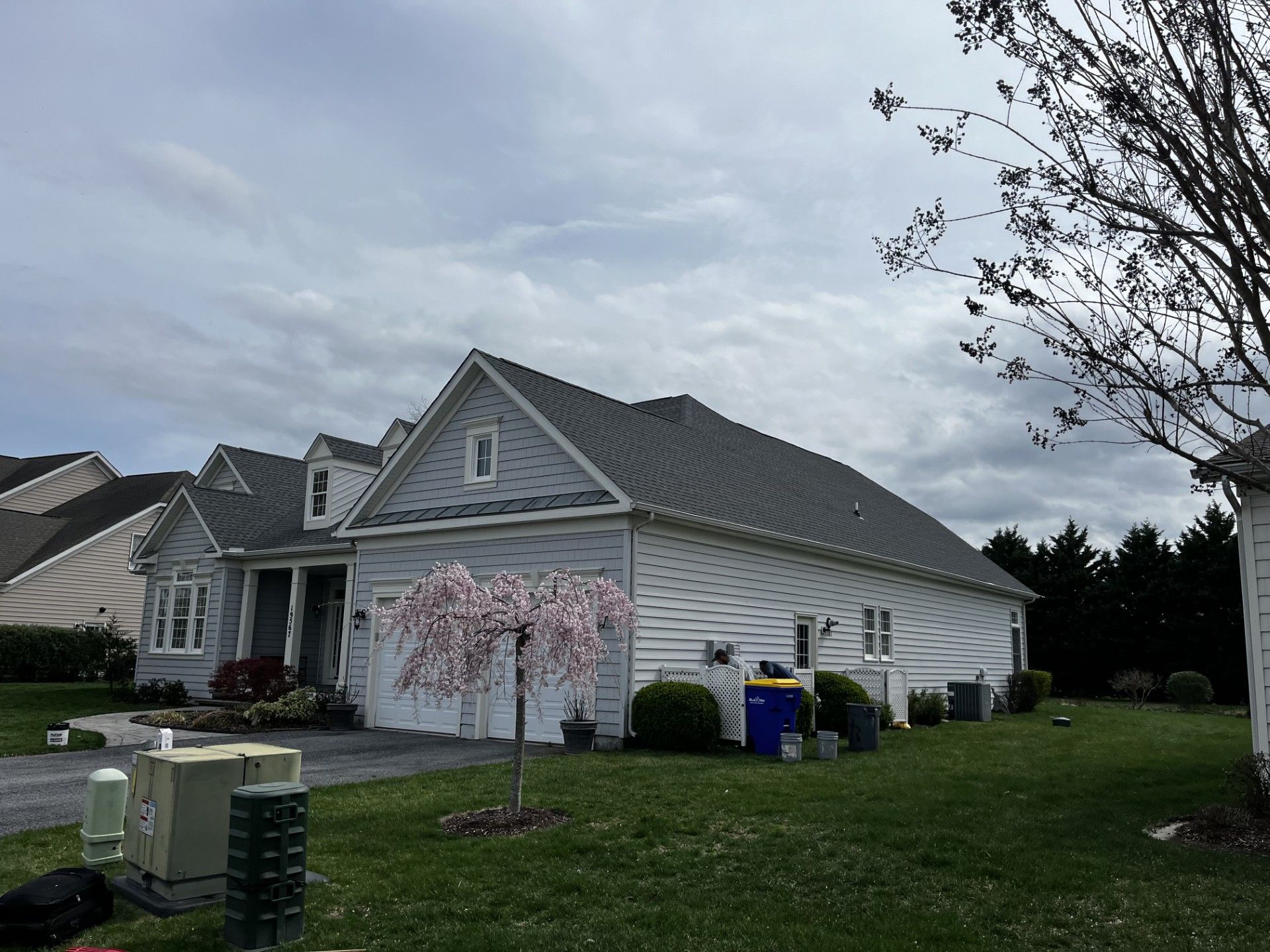 A white house with a gray roof and a tree in front of it