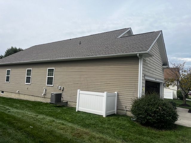 Tan house with gray roof and white trim, green lawn, white fence, garage, and overcast sky.