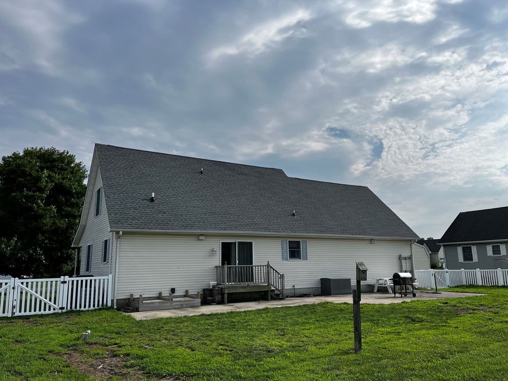 A white house with a gray roof is sitting on top of a lush green field.