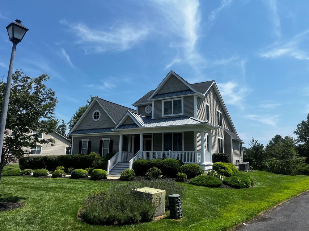A large house with a large porch is sitting on top of a lush green hill