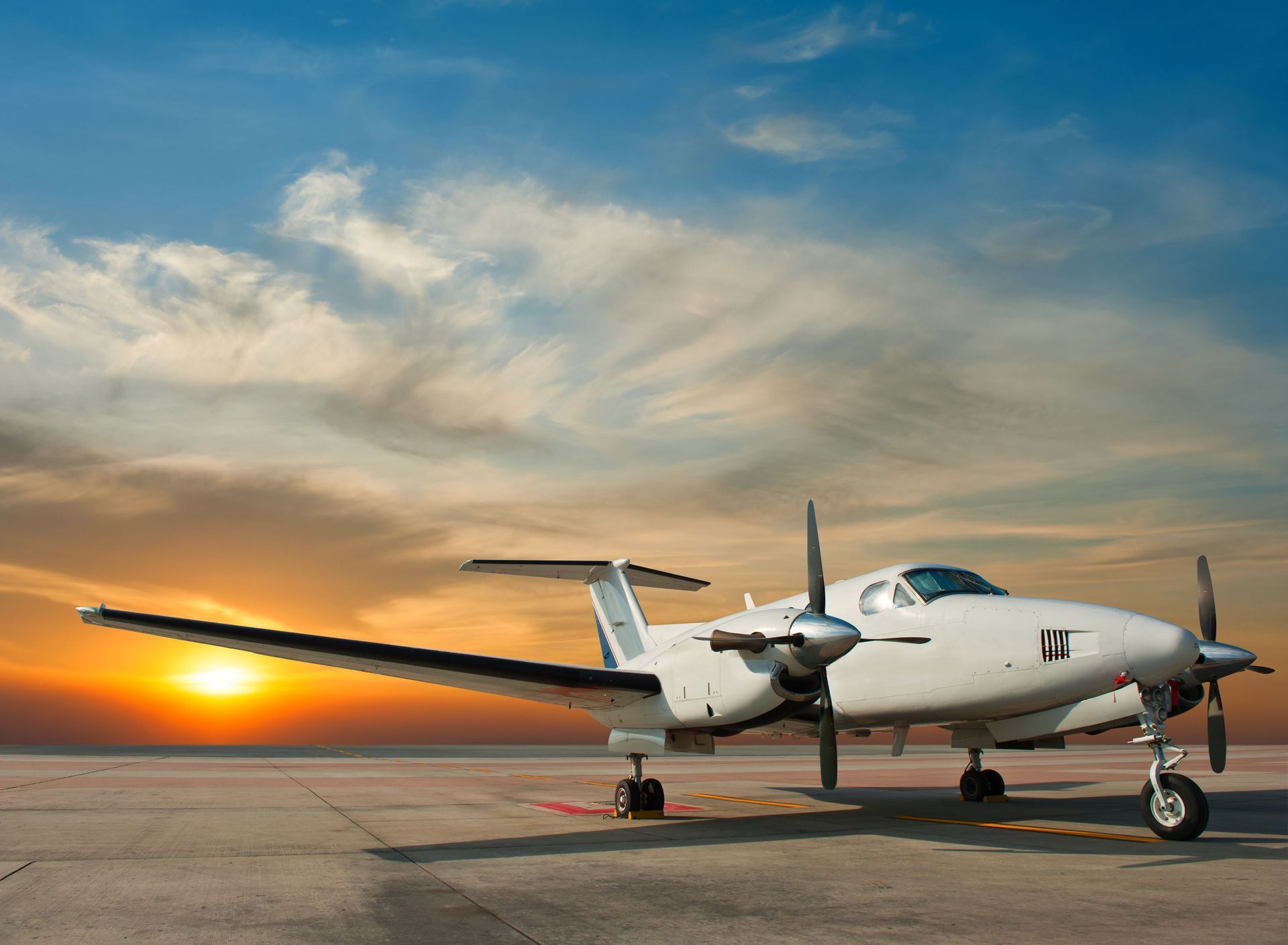 White twin-engine aircraft on a tarmac at sunset, with blue sky and orange horizon.