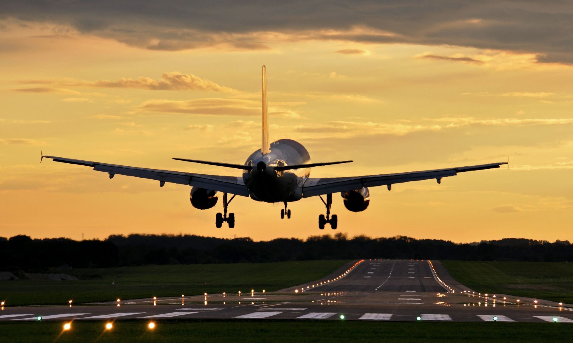 Airplane landing on runway at sunset. Orange sky, green ground, illuminated runway lights.