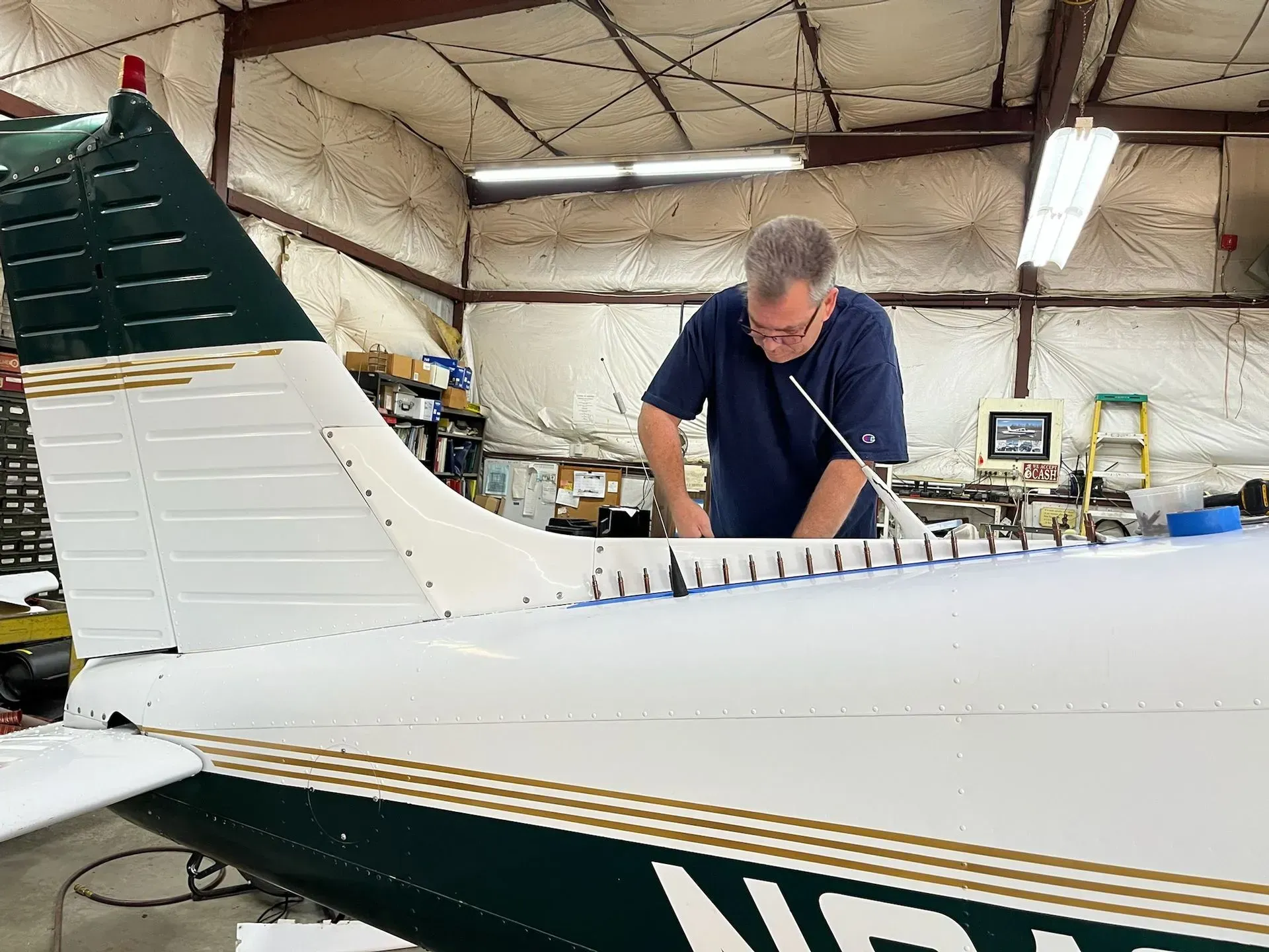 Man working on aircraft tail, white and green with gold trim, inside a hangar.