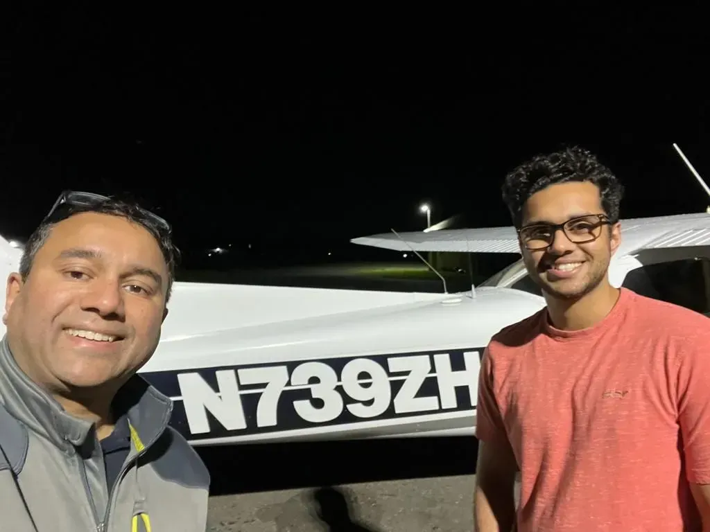 Two men smiling in front of a small airplane at night; registration number N739ZH visible.