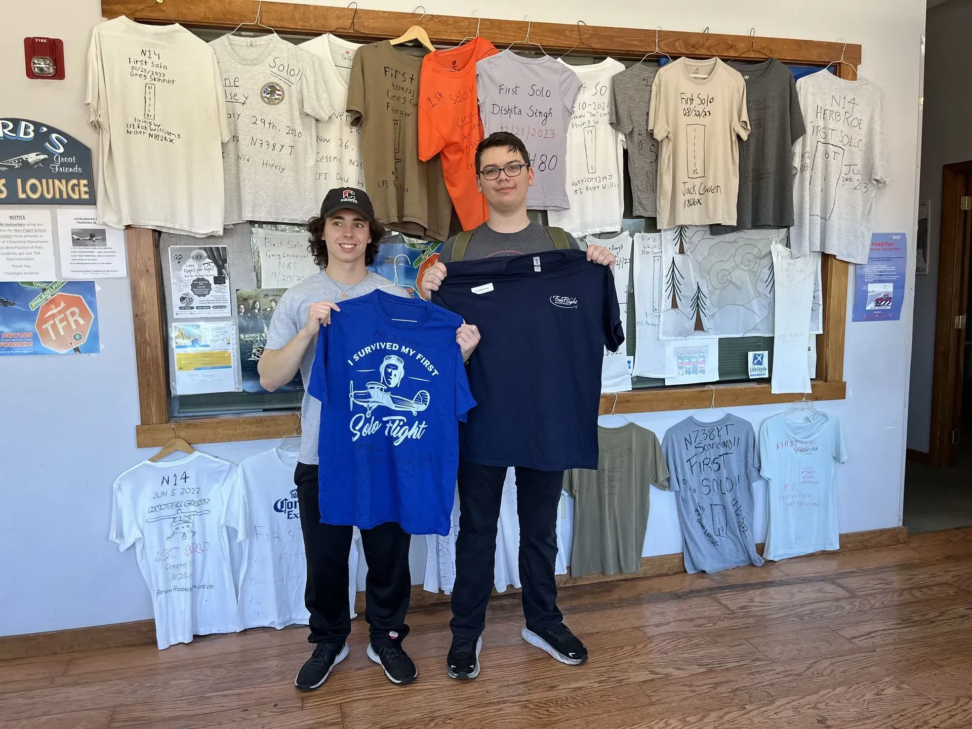 Two people holding up t-shirts in front of a display. Shirts are on display.