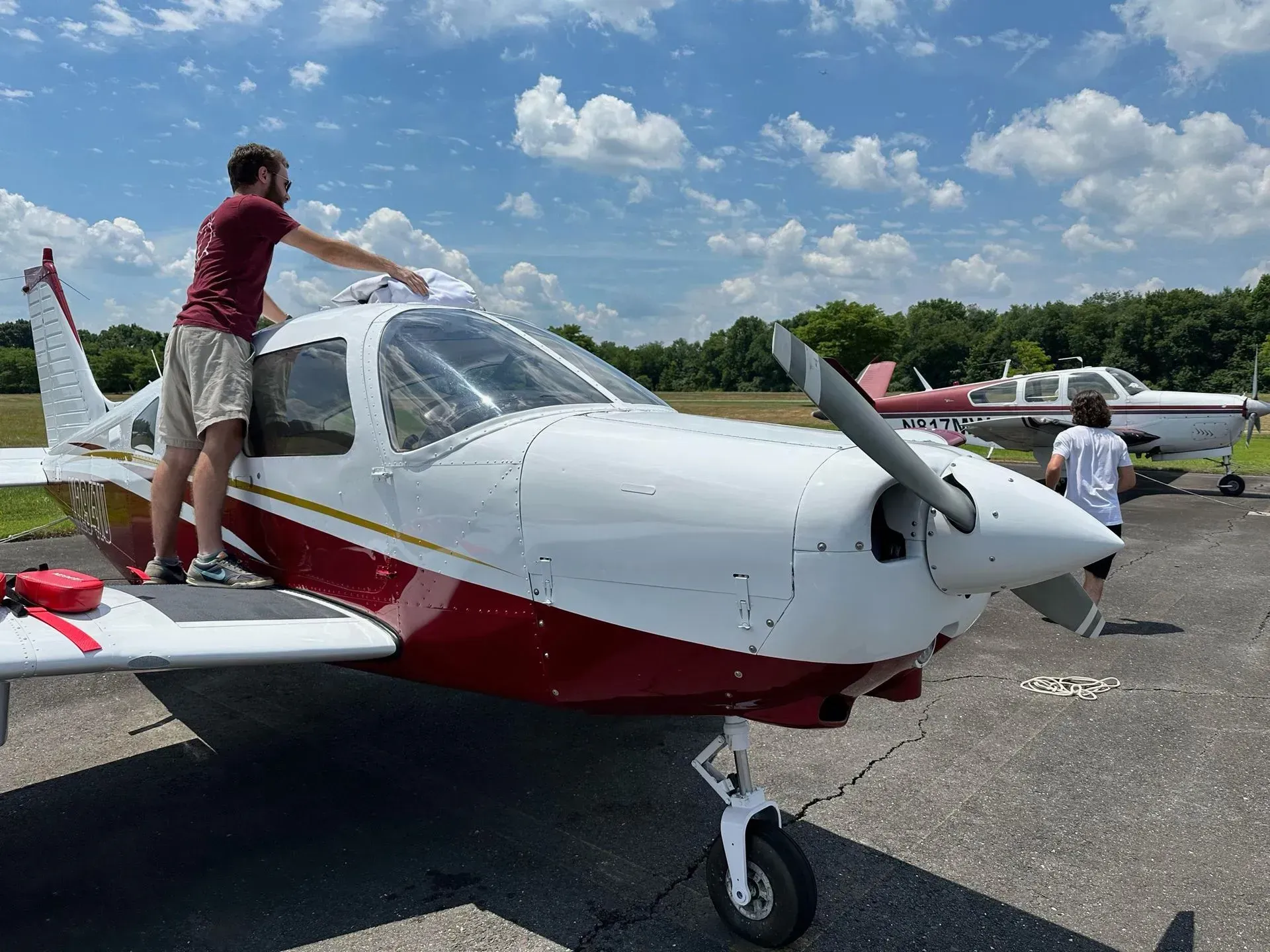 Man on a white and red airplane roof, wiping the windshield on a sunny day.
