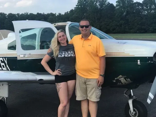 Woman and man standing by a small airplane, posing for a photo at an airport.