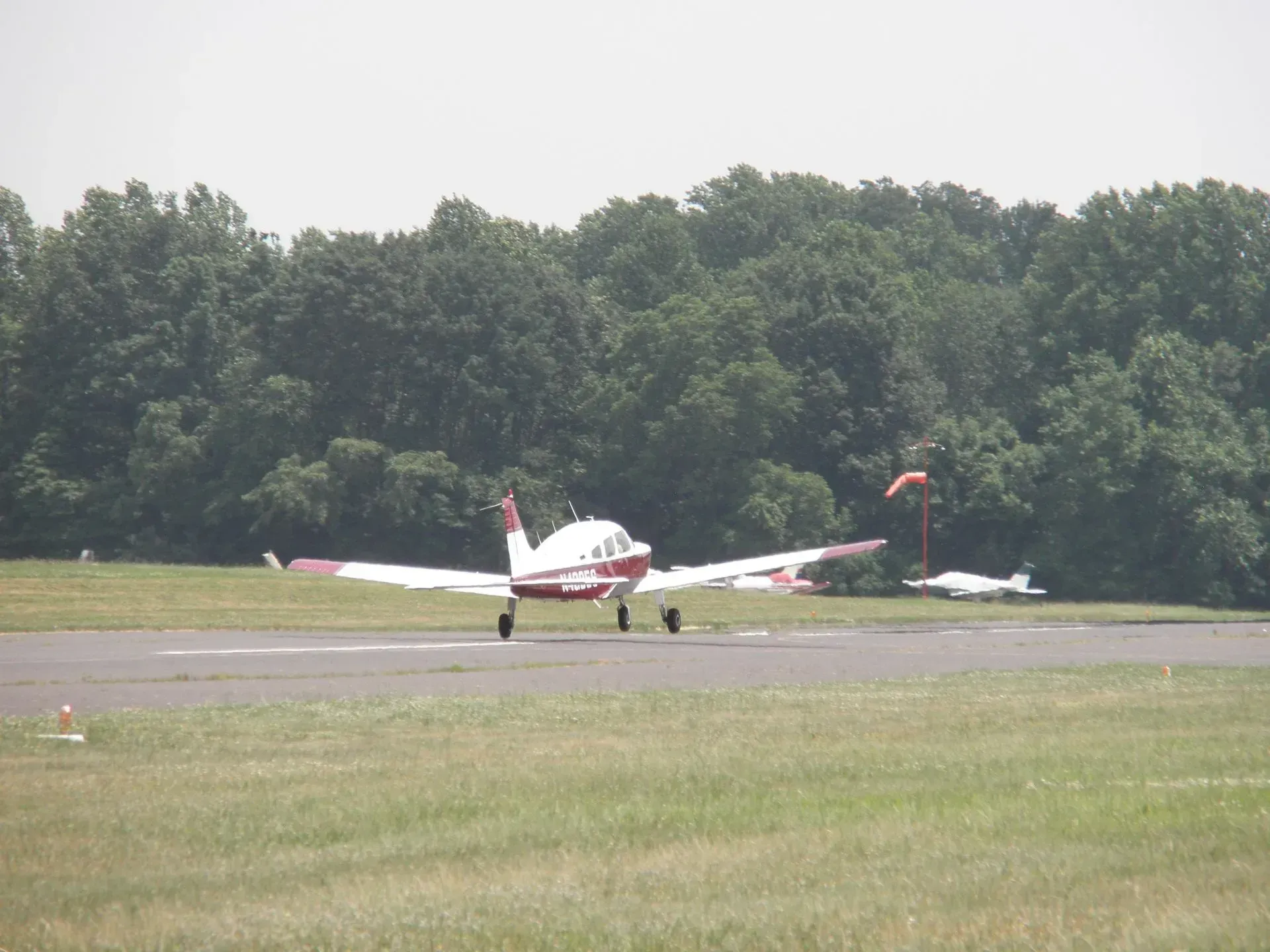 Small, red and white airplane on a runway, preparing for takeoff, with trees in the background.