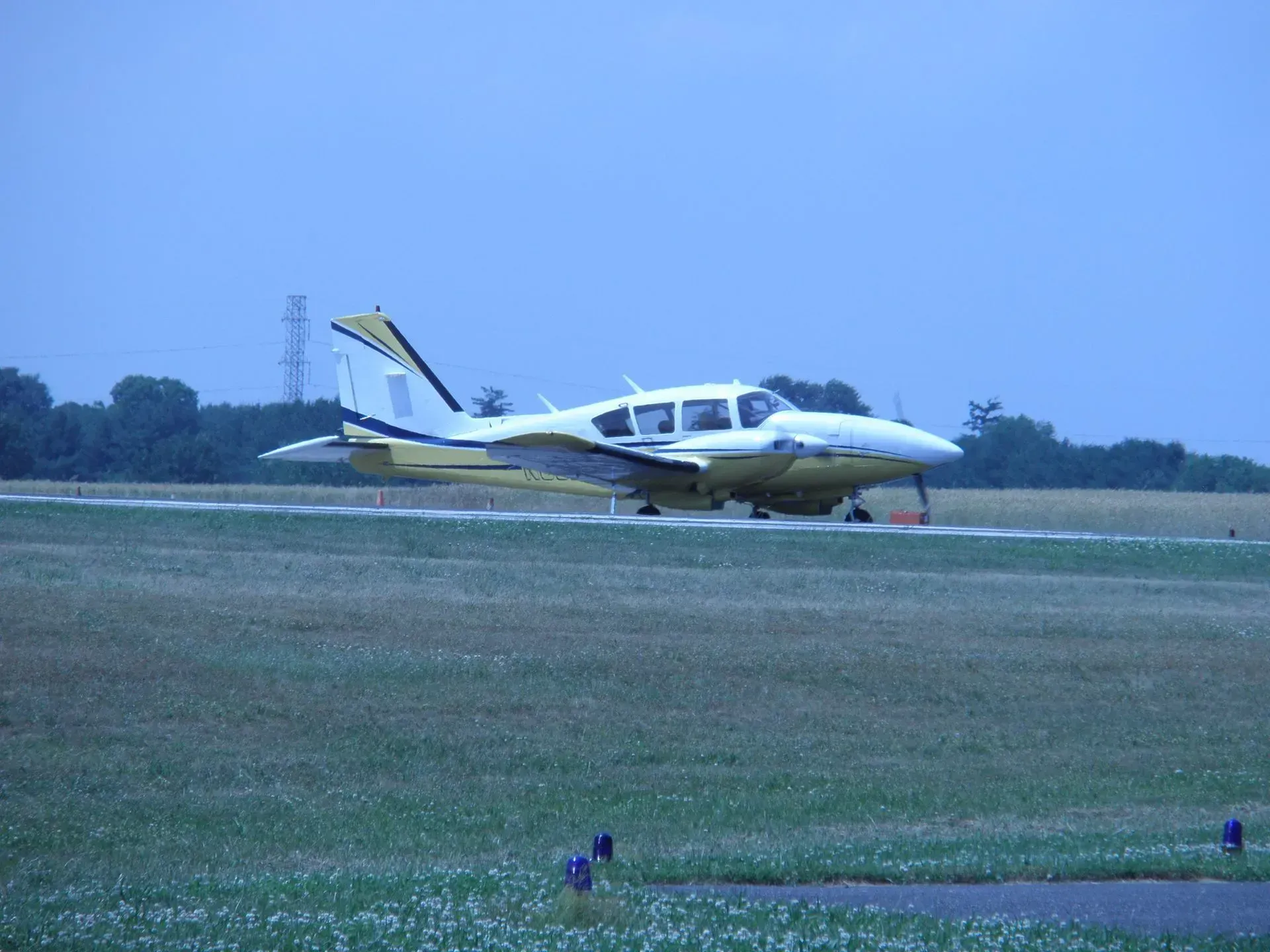 Yellow and white small airplane on a grassy airfield, ready for takeoff under an overcast sky.