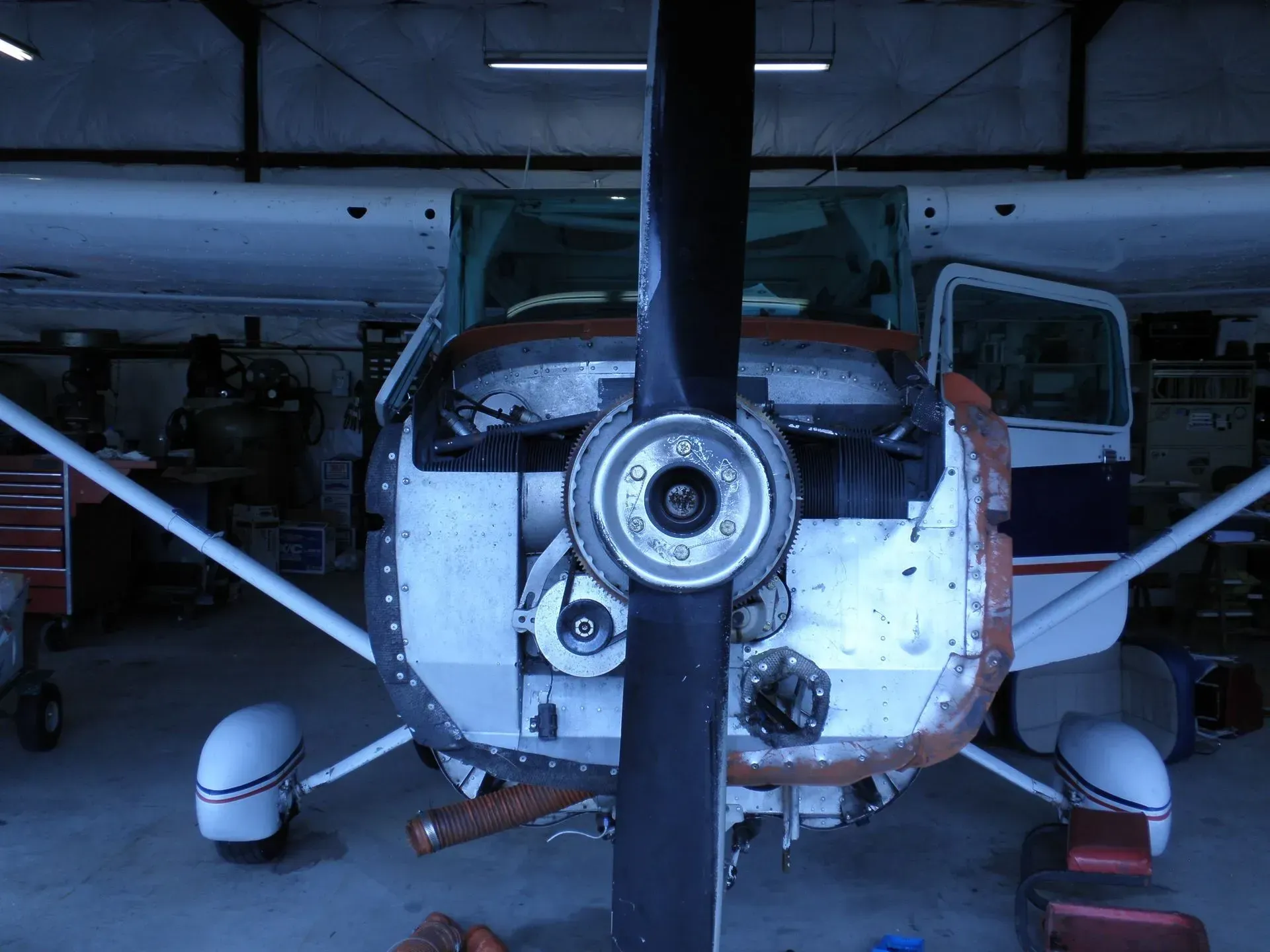 Airplane engine with open panels in a hangar, propeller in the foreground.