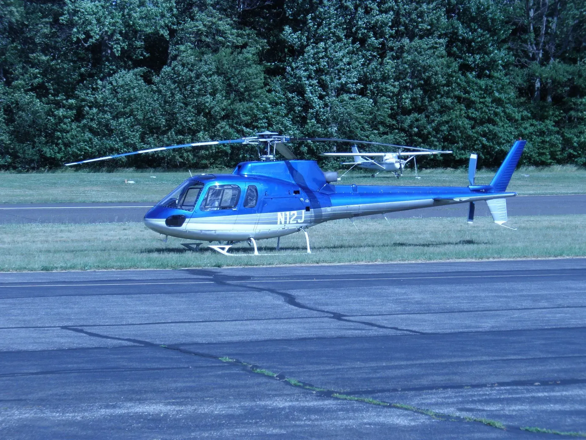 Blue helicopter parked on a tarmac, trees in the background.