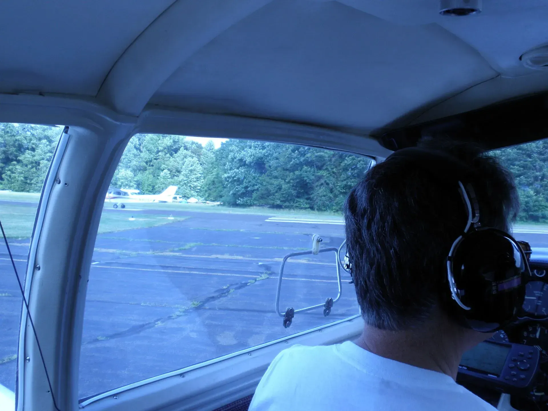 Pilot in cockpit looking out at a small plane on a runway, overcast sky.