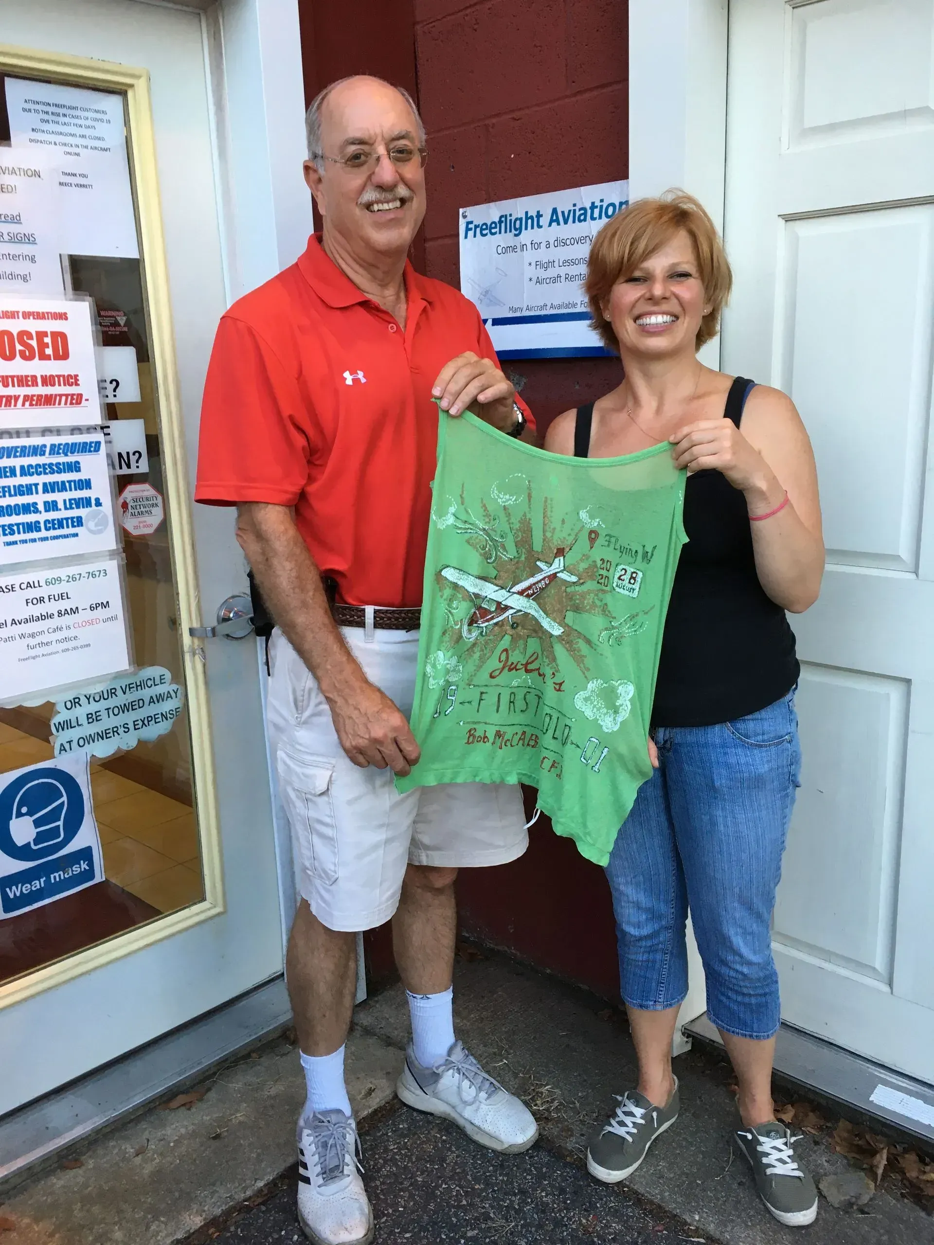 Man and woman holding a green t-shirt with a design, standing in front of a building.