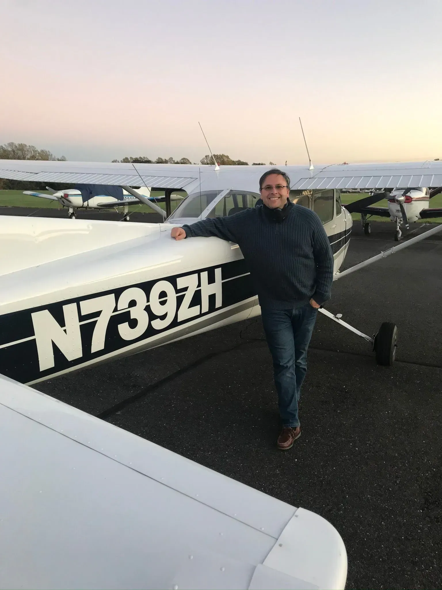 Man leaning on a small airplane, registration number N739ZH, on an airport tarmac.